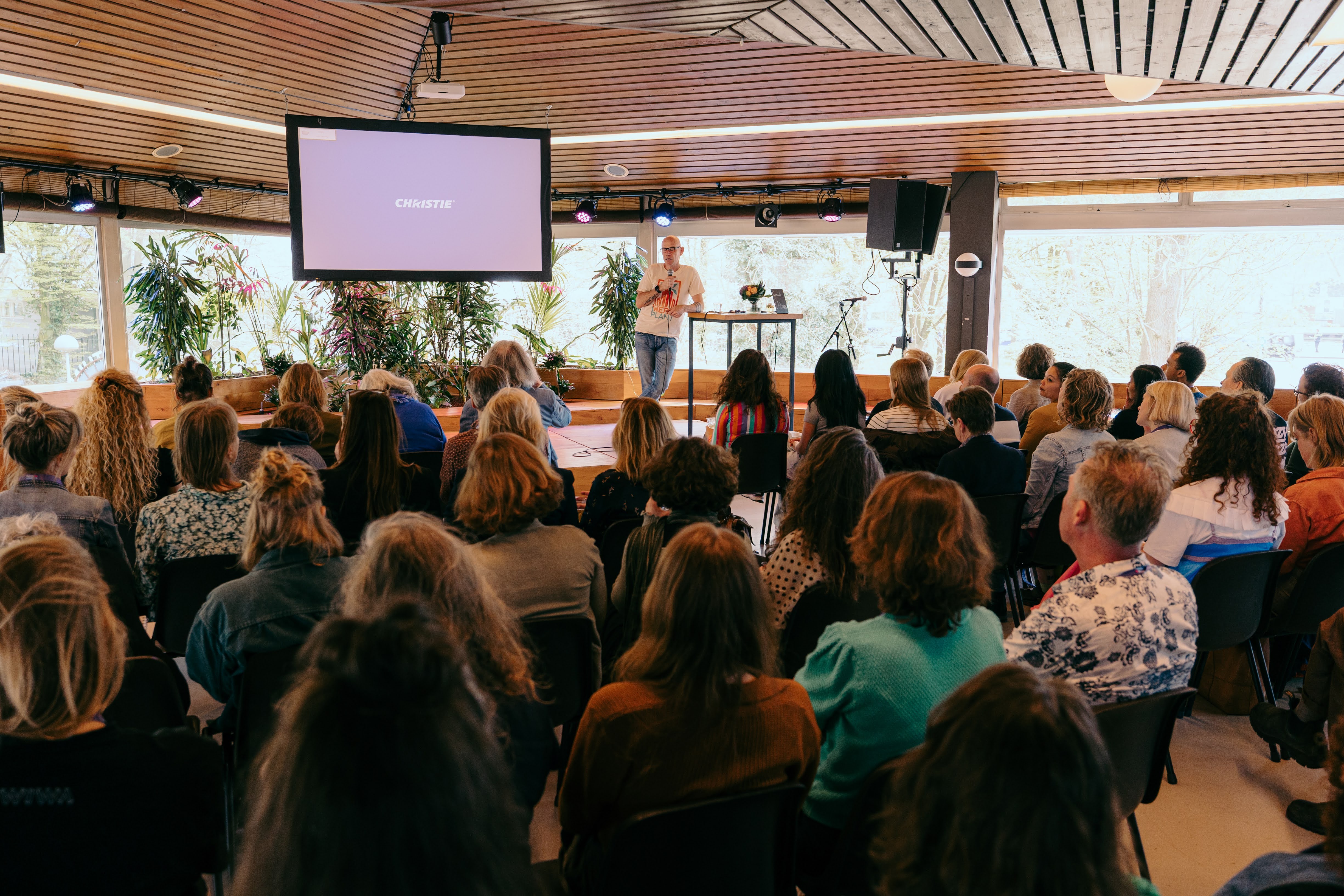 blik op zaal met zittende mensen die kijken naar een man op een podium